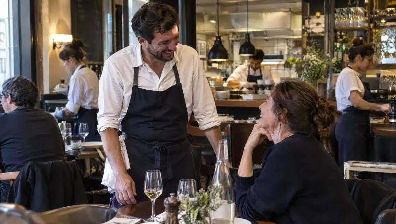 Un serveur échange en souriant avec un client habitué pendant le déjeuner
